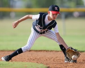 Youth pitching athlete catching a baseball on the ground