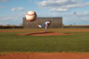 Baseball flying toward the camera with youth pitching player in the background.